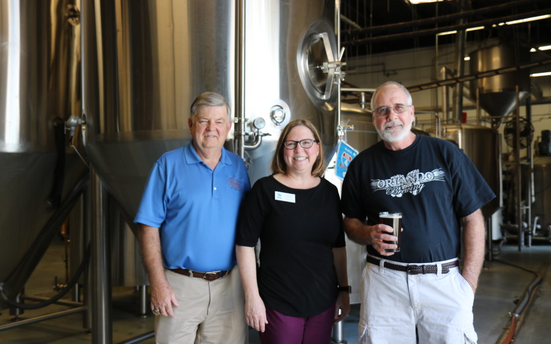 Habitat CEO Catherine McManus poses with two men from Orlando Brewing at the brewery.