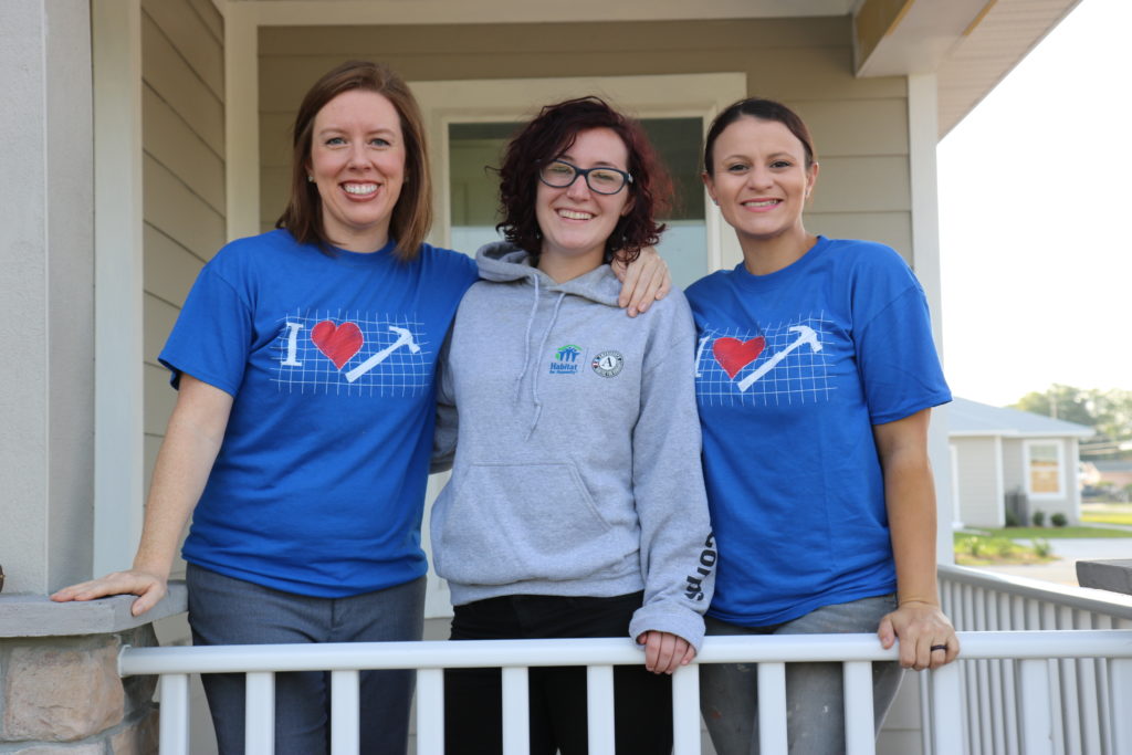 Past AmeriCorps volunteers pose on the porch of a brown Habitat Orlando & Osceola home.