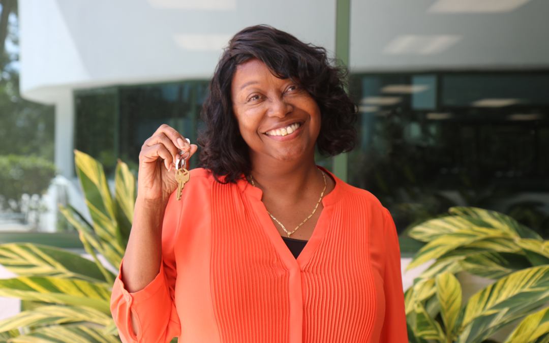 Woman smiling standing in front of plants holding key