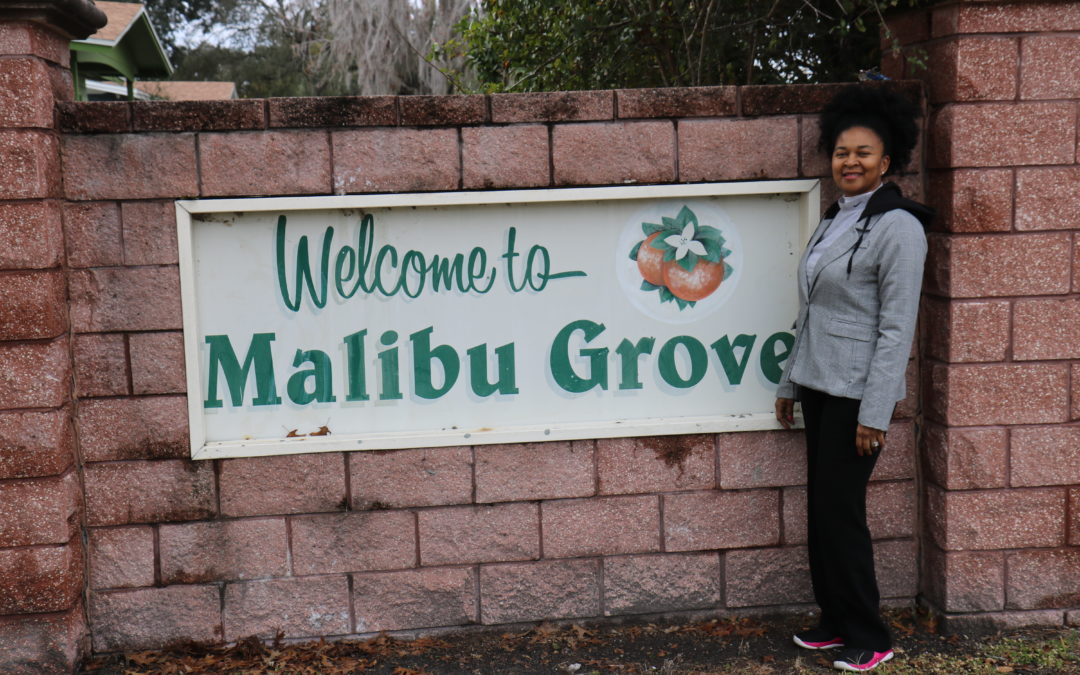Woman smiling in front of brick wall and "Welcome to Malibu Groves" sign