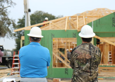 Two men wearing hard hats looking at in-progress house