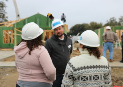 Women talking to man wearing hard hat in front of two under-construction homes
