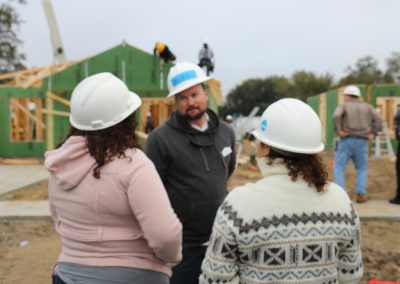 Women talking to man wearing hard hat in front of two under-construction homes