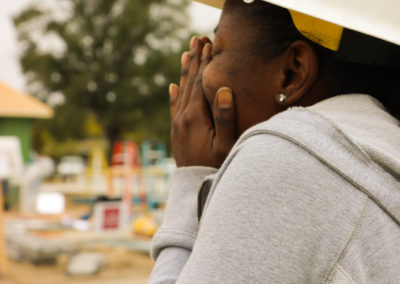 Woman wearing hard hat and covering her face with her hands as she looks at her house being constructed