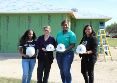 Four women holding hard hats and smiling in front of in-progress house
