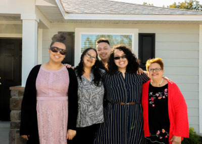 Family of five people smiling in front of completed house