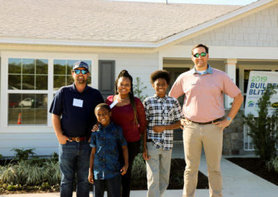 Two men, a women and two boys smiling in front of completed home