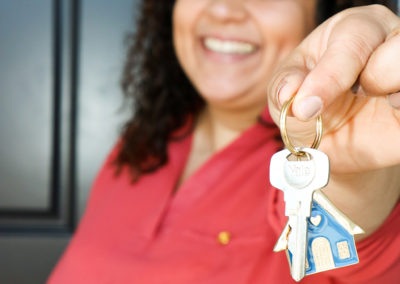 Woman smiling in front of black door and holding out house-shaped keychain