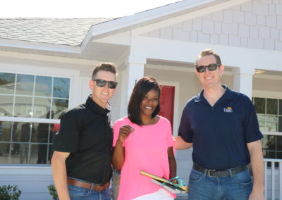 Two men and woman smiling in front of completed house