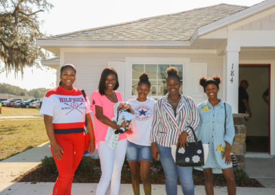 Five women smiling standing in front of completed house with open front door