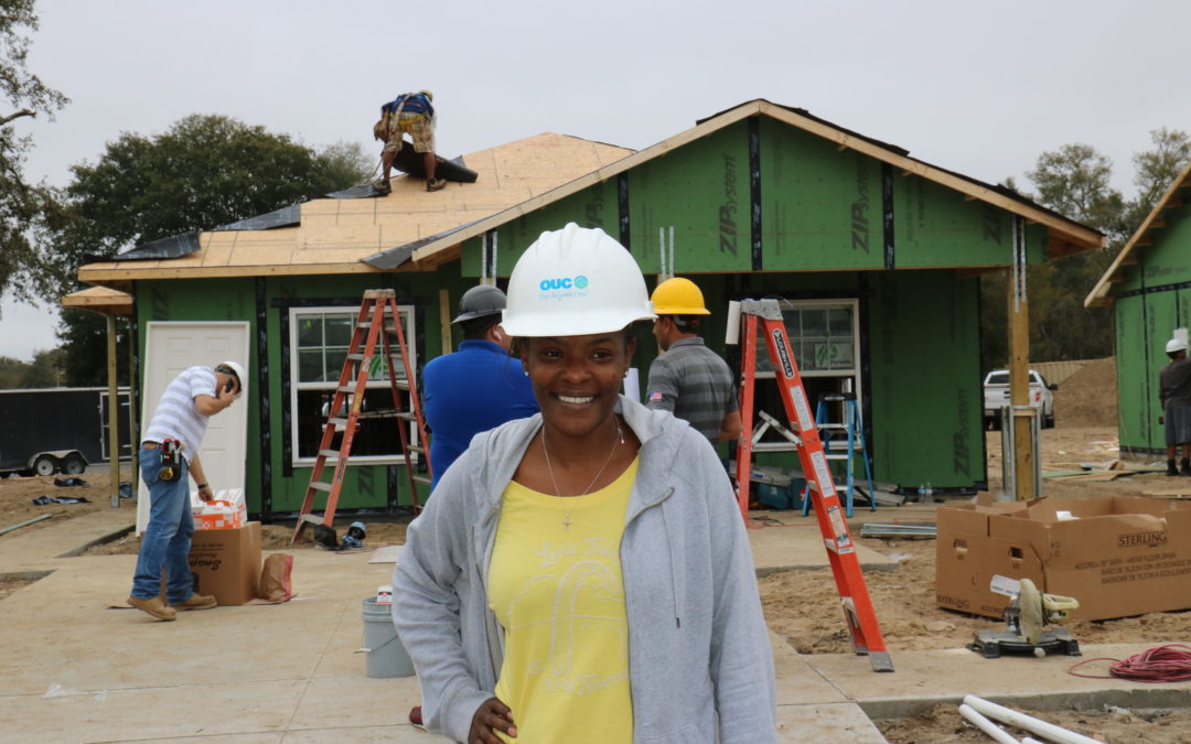 Mulher usando mão dura e sorrindo em frente a uma casa em construção