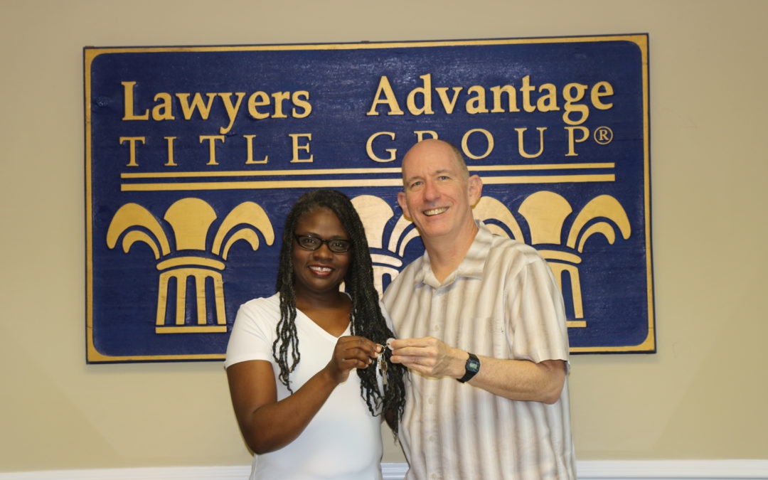 Woman and man smiling holding keys in front of Lawyers Advantage Title Group sign