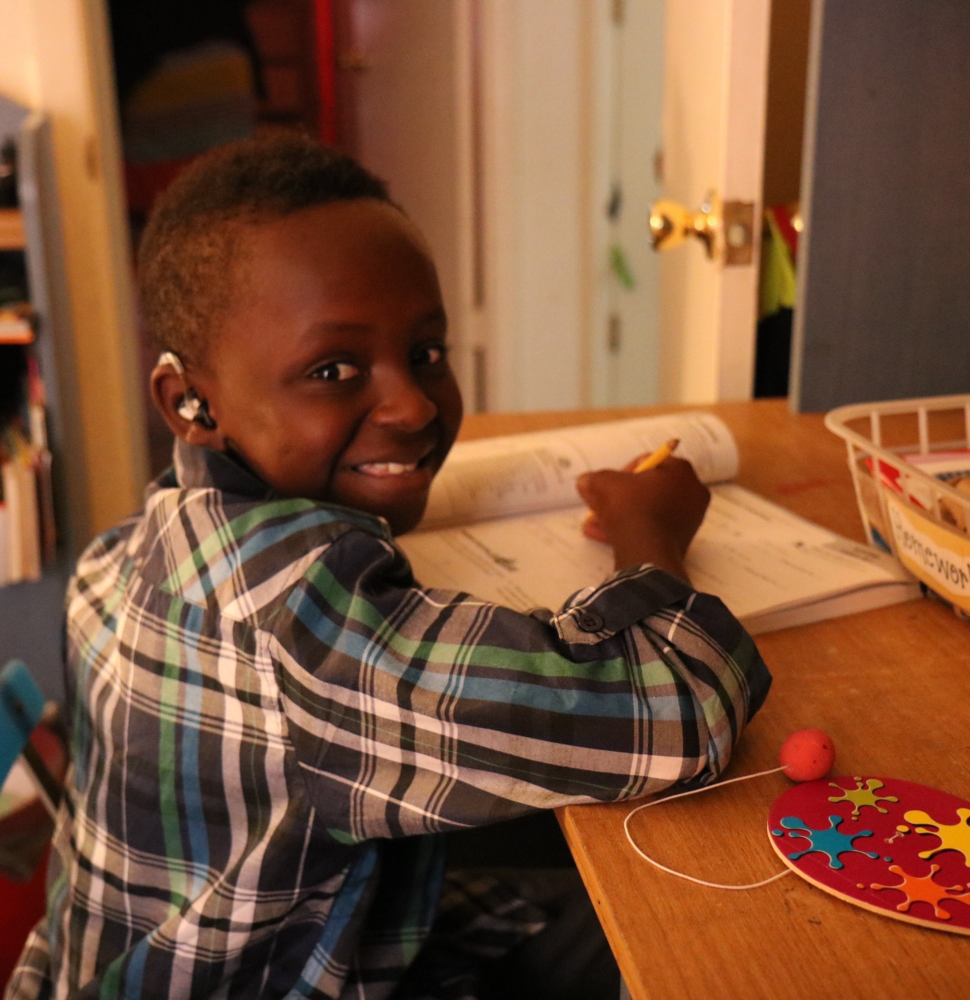 Joven sonriendo y sosteniendo un lápiz sobre un cuaderno de ejercicios en la mesa de la cocina