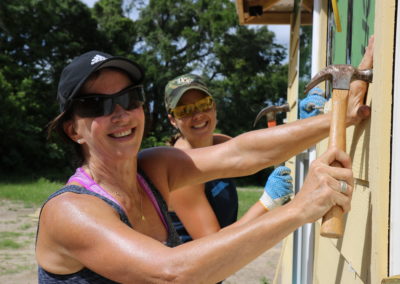 Two women smiling and installing siding on house
