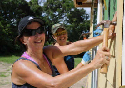 Two women smiling and installing siding on house
