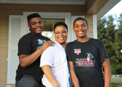Woman and two teenage boys smiling in front of completed home
