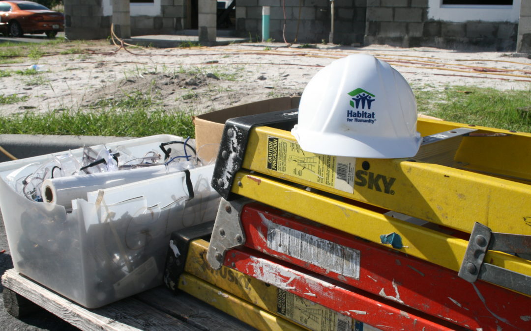 Pile of ladders with white construction hat on top and clear plastic bin with goggles and paper towels inside
