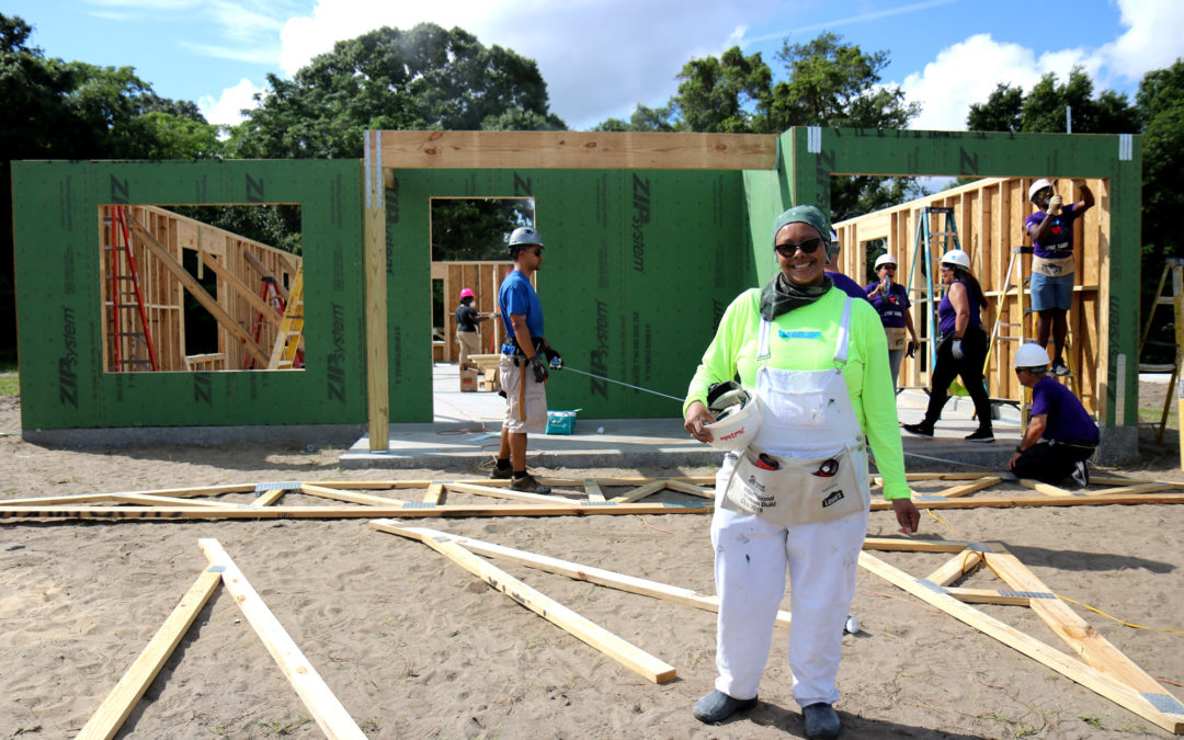 Woman smiling in front of group of people working on in-progress house