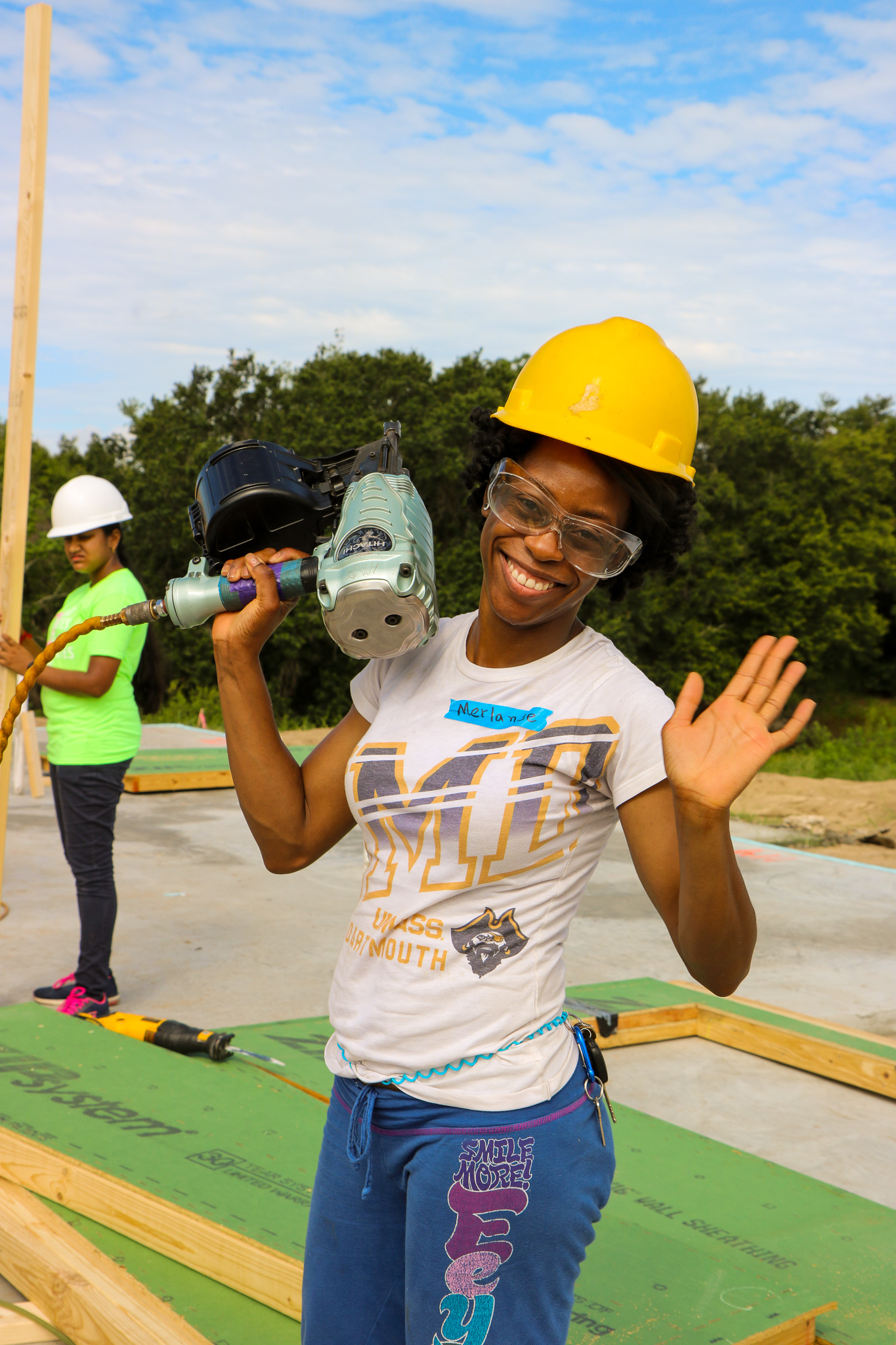 Smiling woman wearing construction hat and protective goggles and holding a nail gun