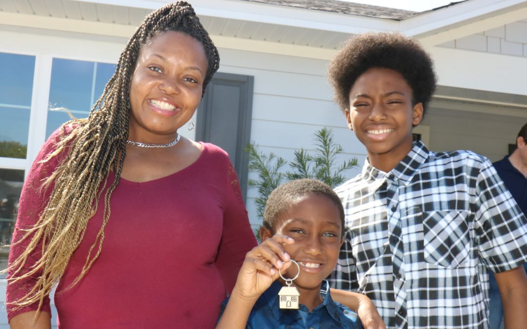 Família de mãe e dois filhos com o mais novo segurando um chaveiro de casa em frente à sua casa completa