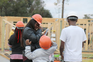 Family of a women, a teenager and two children wearing hard hats with unfinished home in background