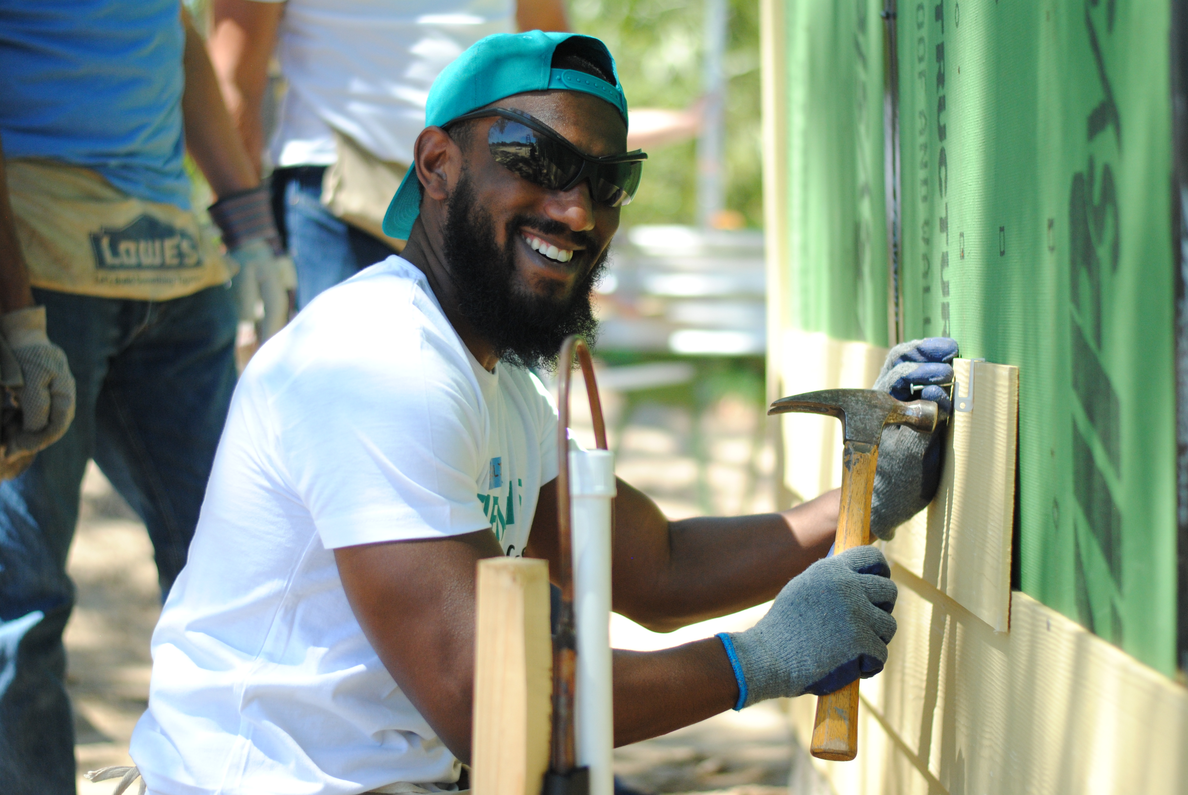 Smiling volunteer installing siding outside in-progress home