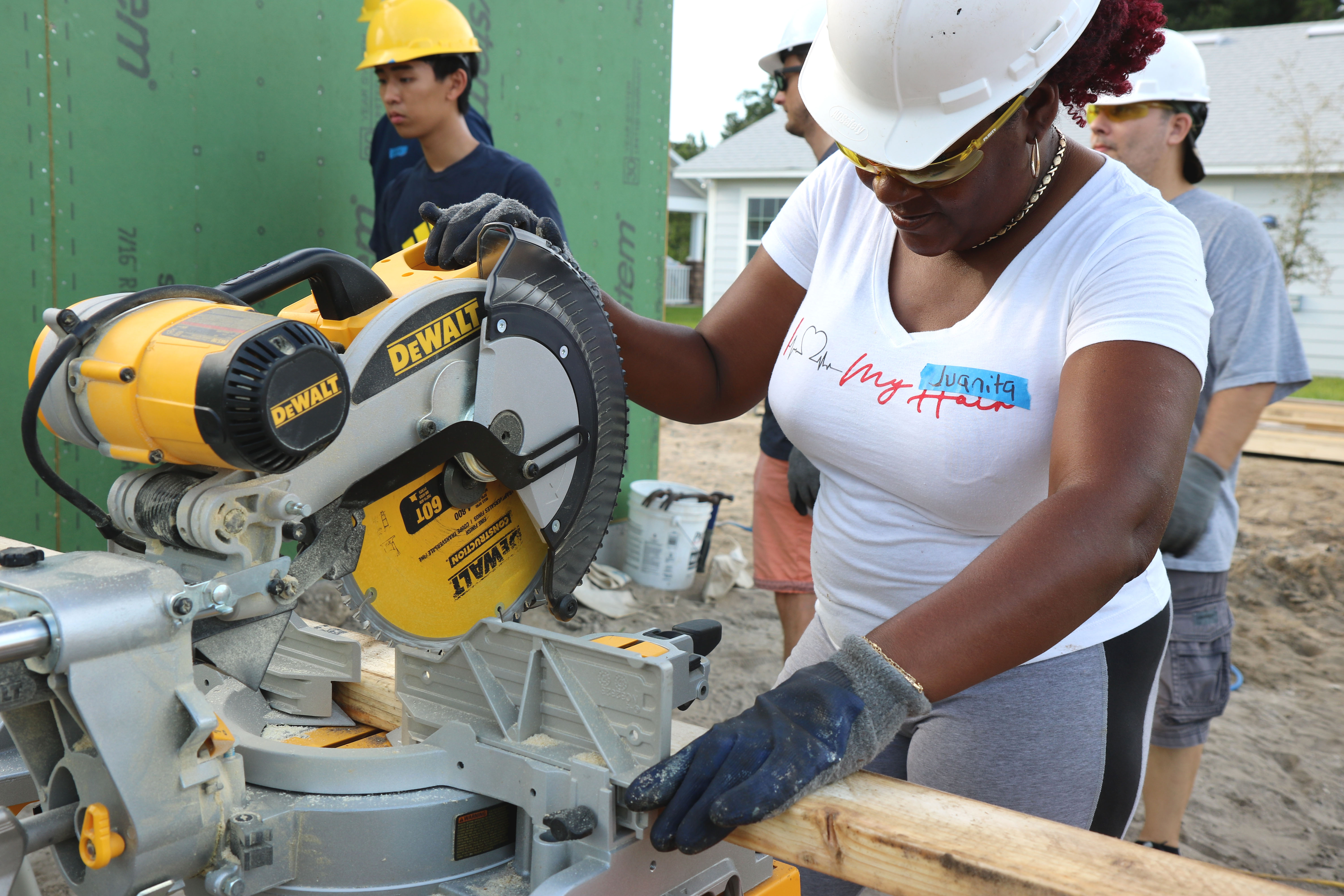 Woman wearing hard hats and glasses, using power saw on build site