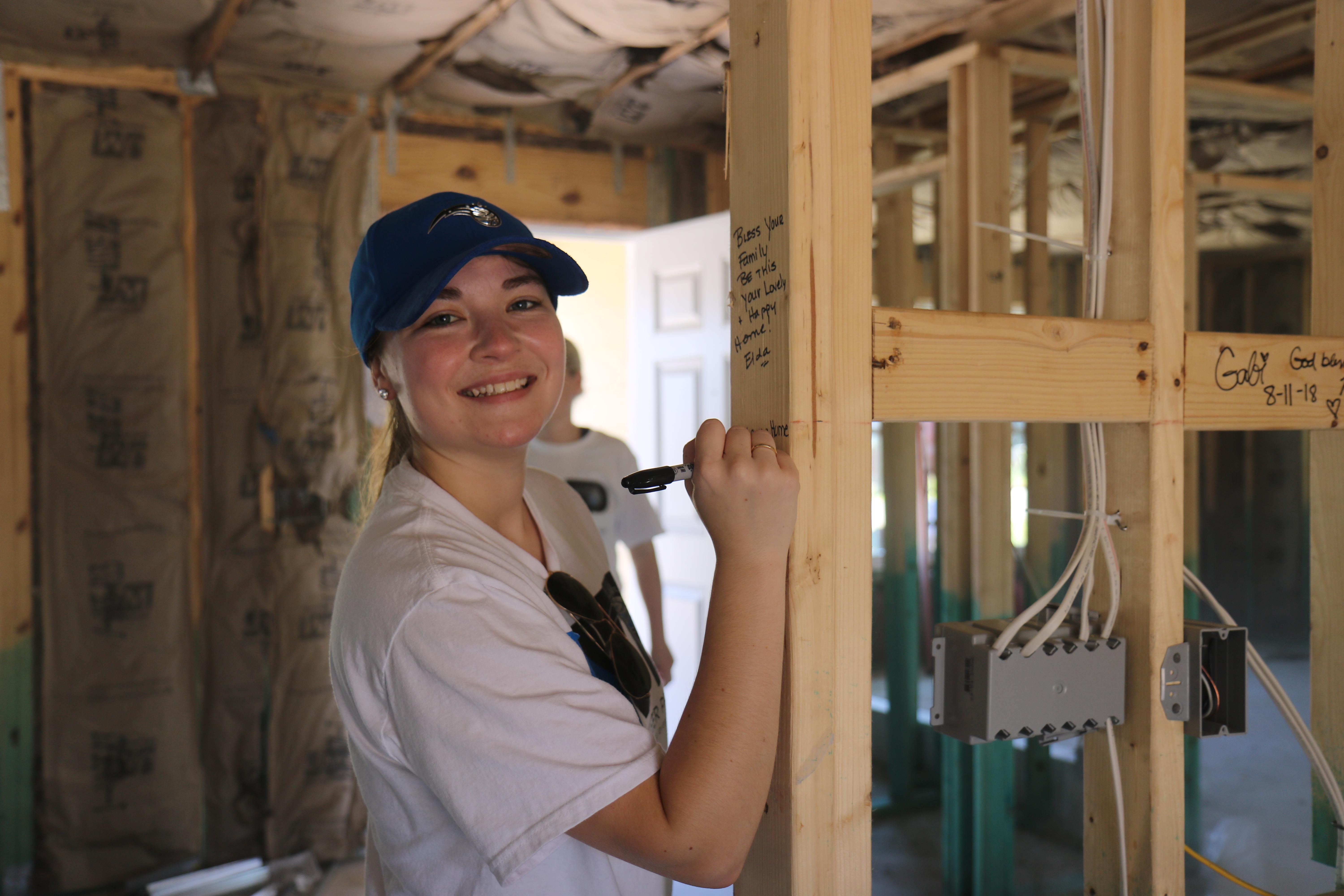 Smiling volunteer writing a blessing on interior beam of in-progress home