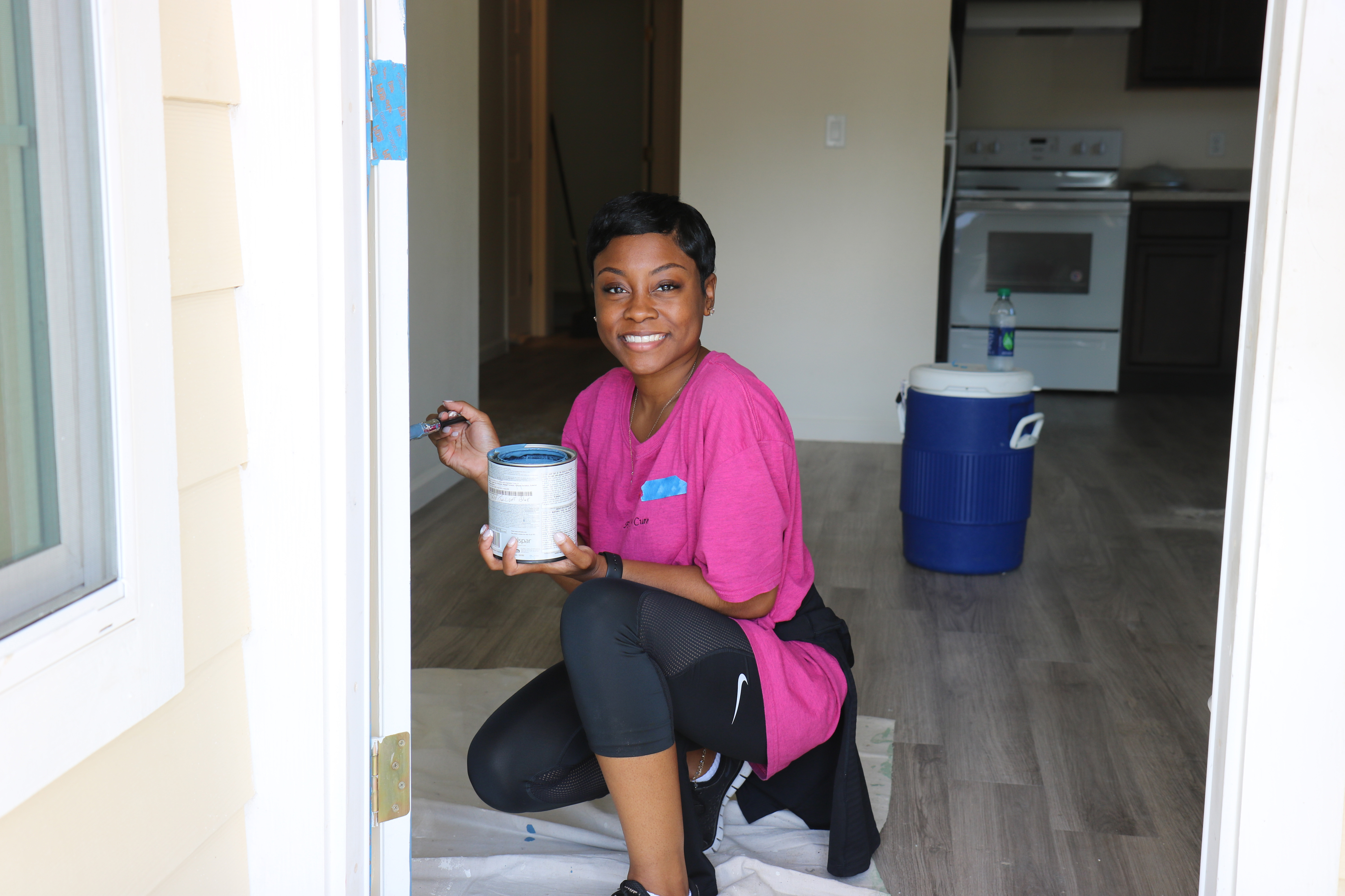Smiling volunteer painting interior door frame with blue cooler and kitchen in background