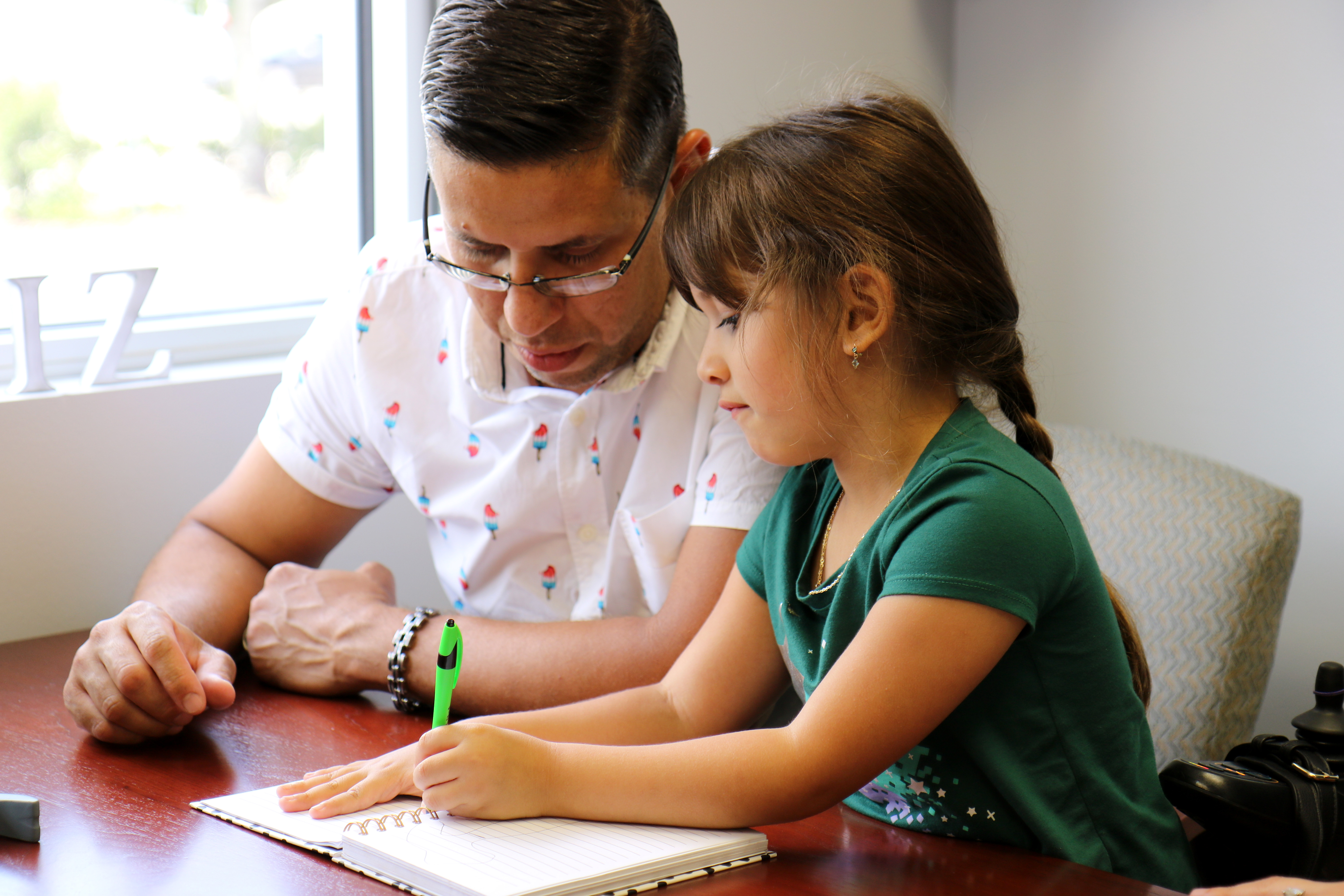 Man and young girl drawing at a desk and looking down