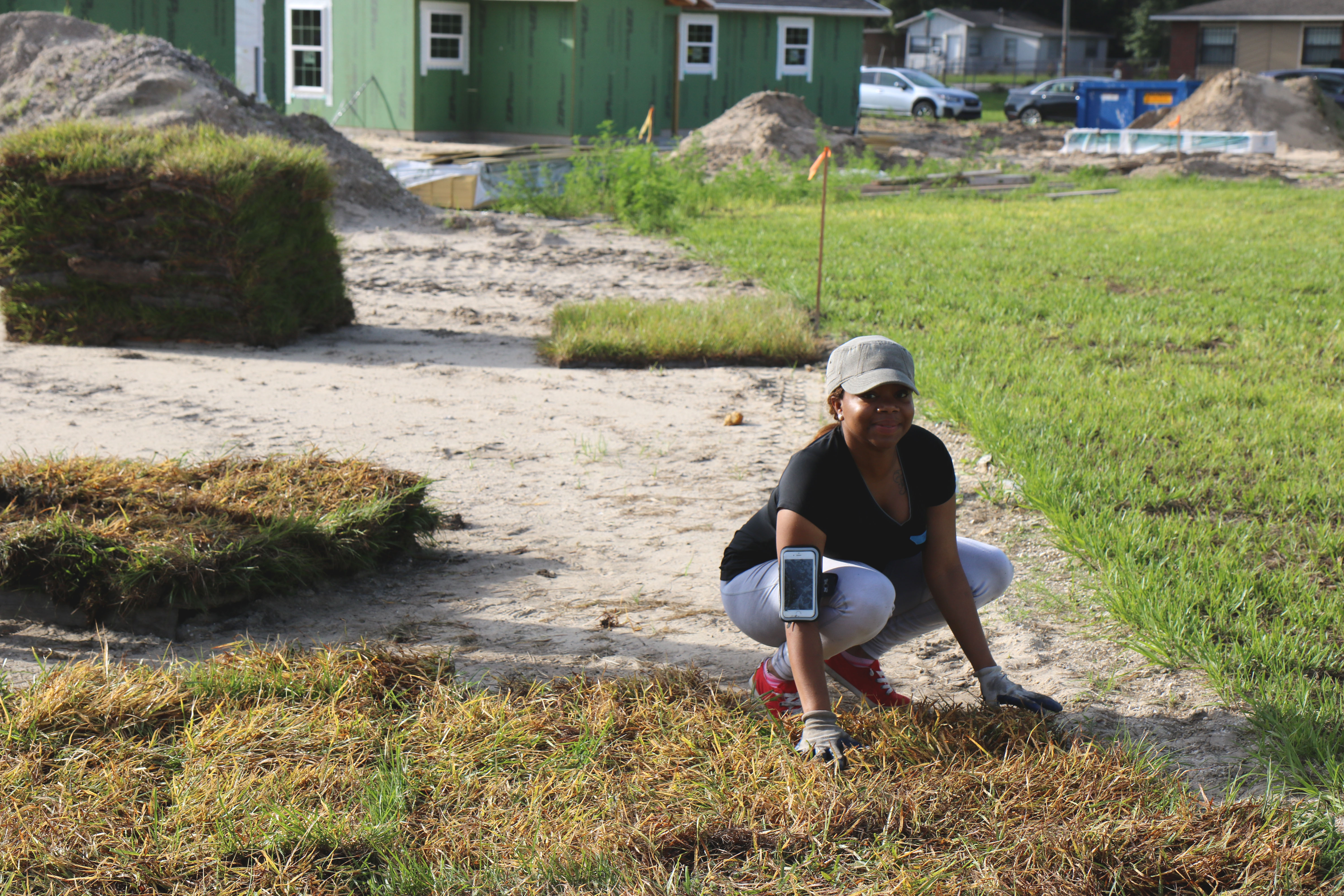 Smiling volunteer crouched laying sod on build site