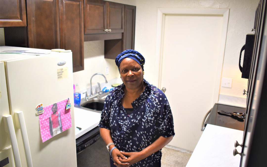 An older woman stands in her kitchen.