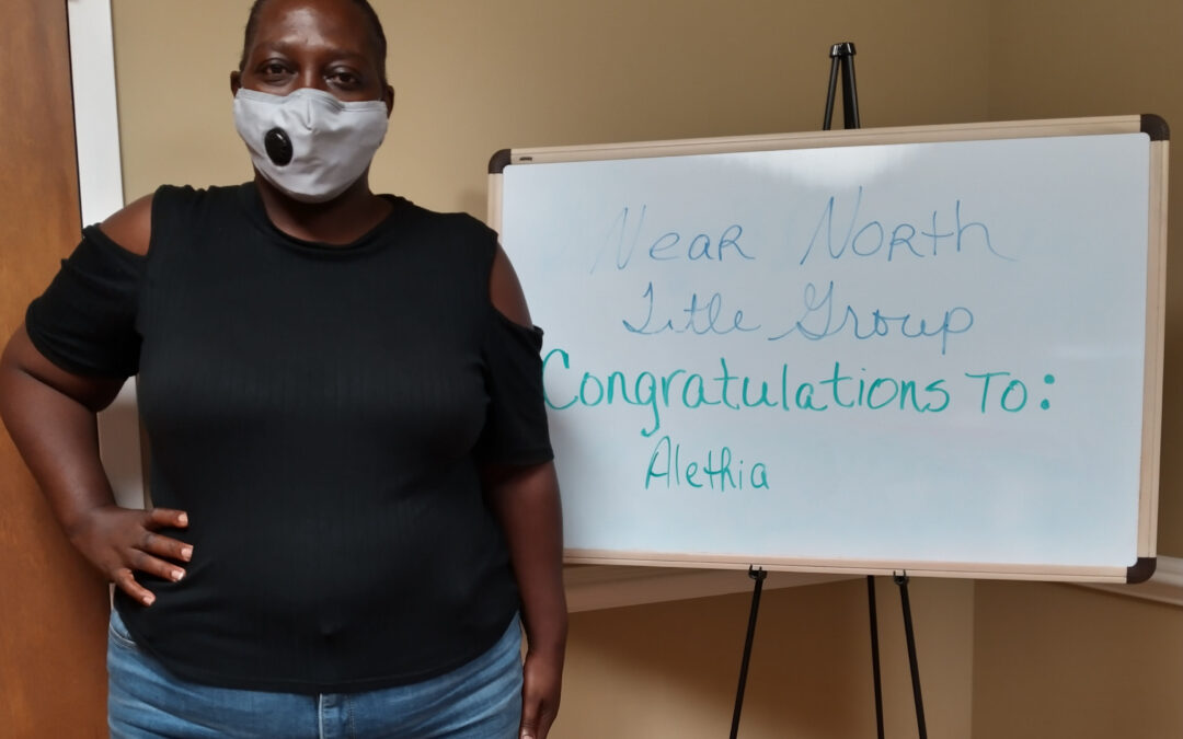 A masked woman poses in front of a sign that reads, "Near North Title Group congratulations to: Alethia"