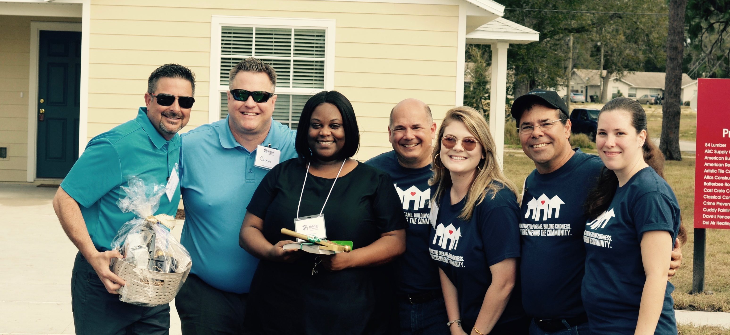 Group of people smiling in front of newly completed house, included a woman and HGR team members