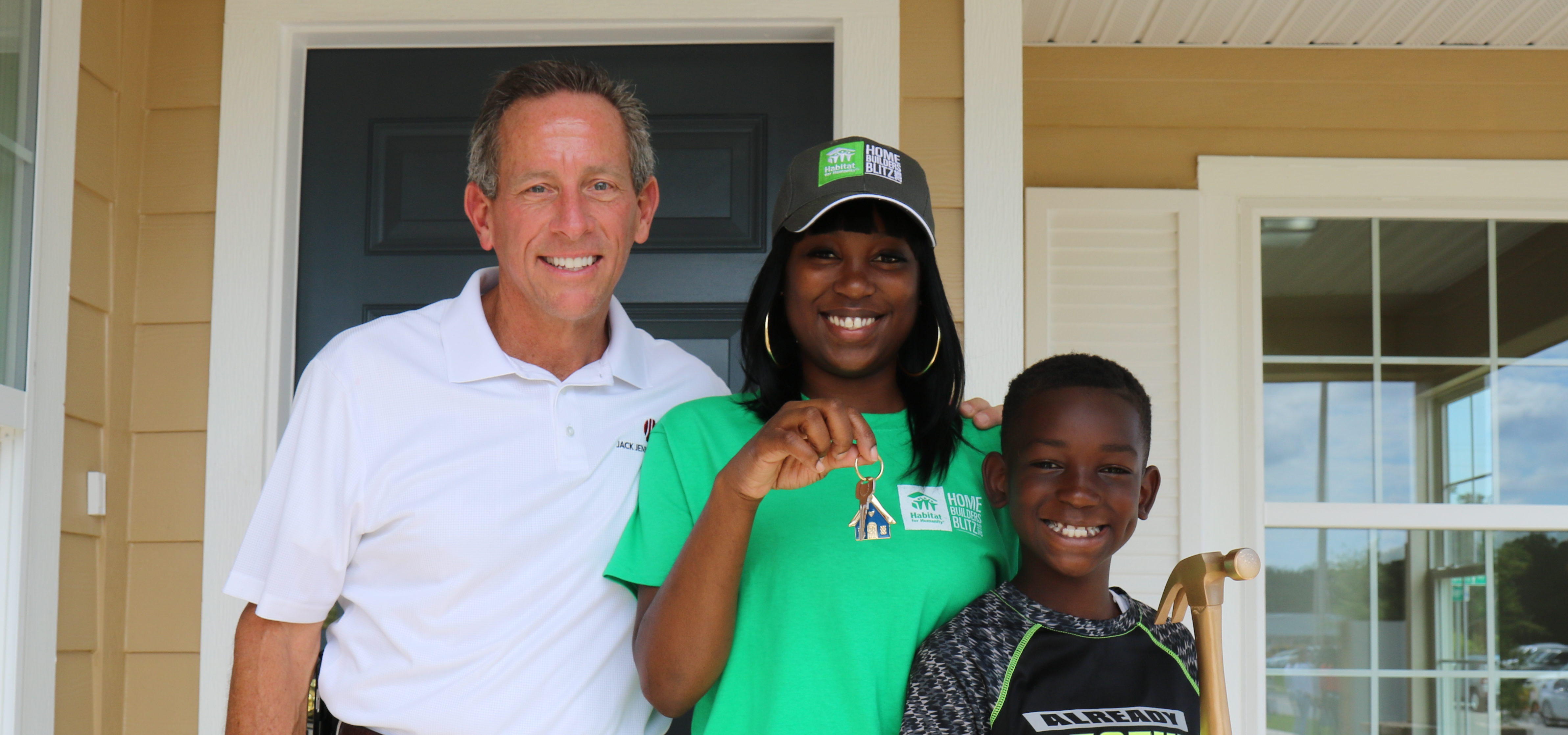 Man, and woman with her young son smiling in front of the door of her newly completed house