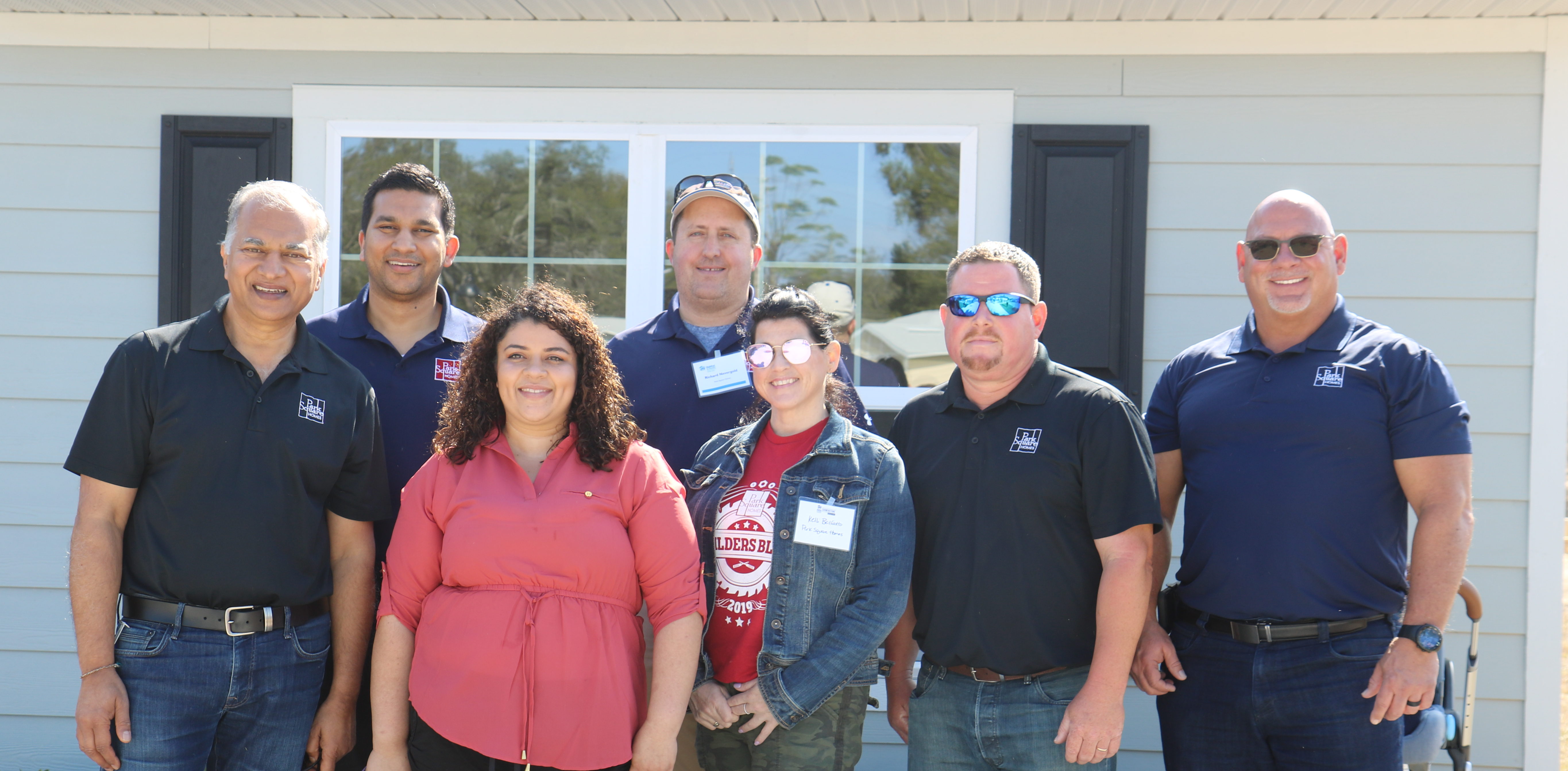 Woman holding leashes of two small dogs, surrounded by Park Square team members in front of her newly completed house