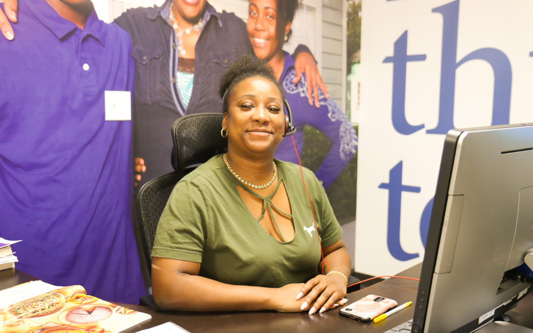 woman smiling and sitting behind computer at front desk of office