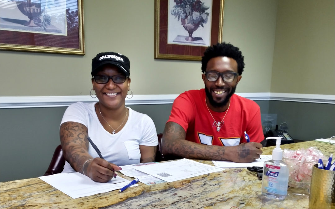 A woman and man smile at the camera during their home's closing.