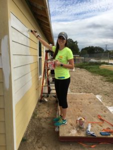 woman smiling and reaching up to paint house