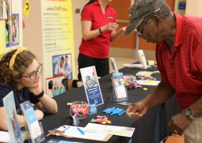 Man standing in front of informational table and speaking with a women sitting thoughtfully