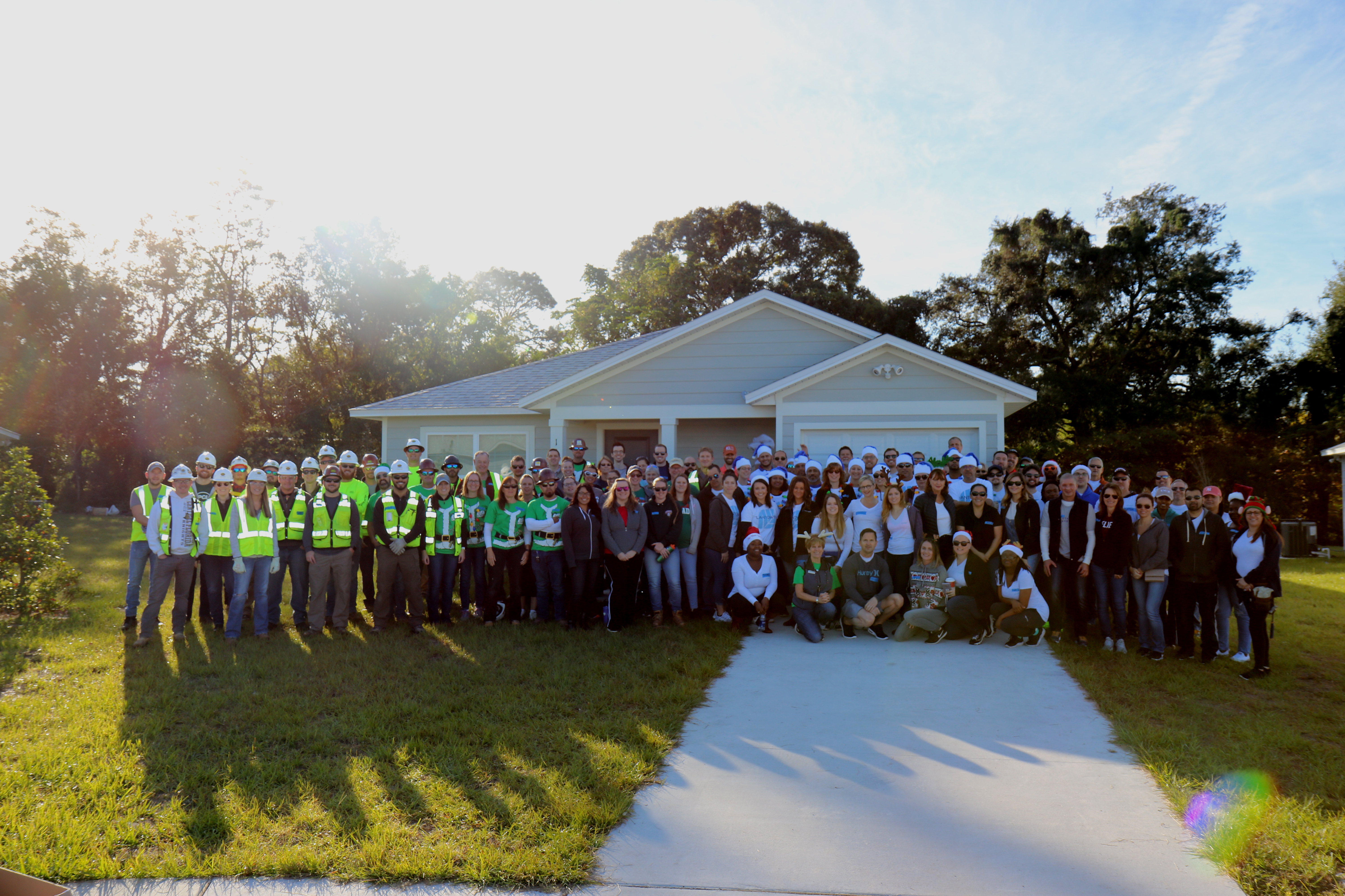A large group of volunteers poses in front of a house.