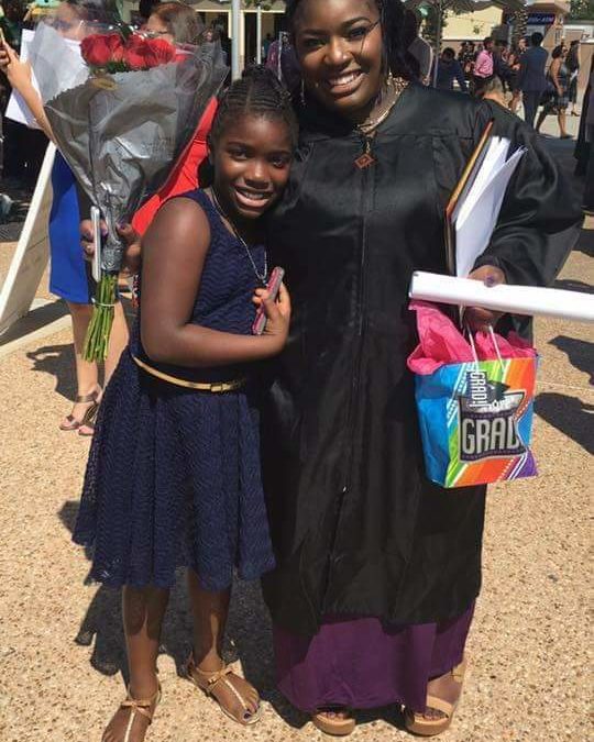 A mother dressed in graduation robes hugs her young daughter.