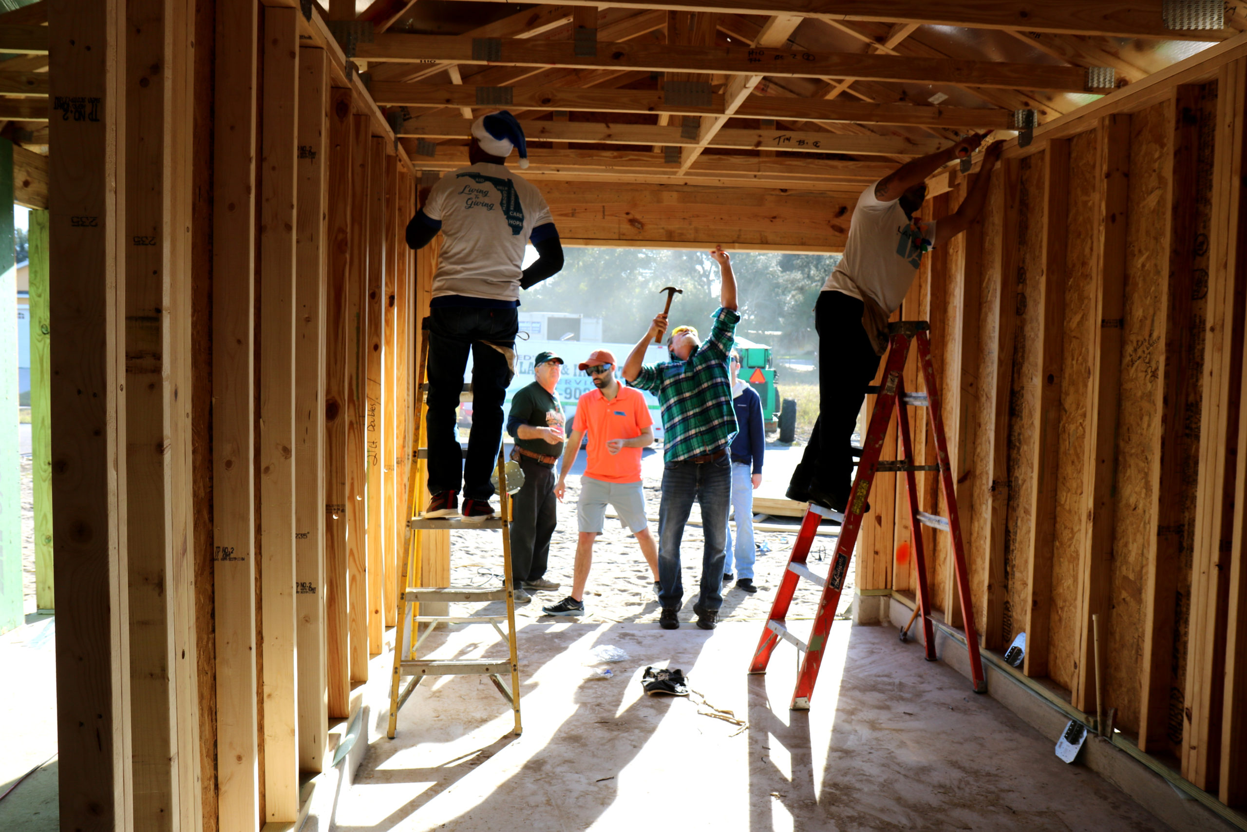 Group of volunteers standing on ladders and reaching up to complete various tasks with tools in in-progress house