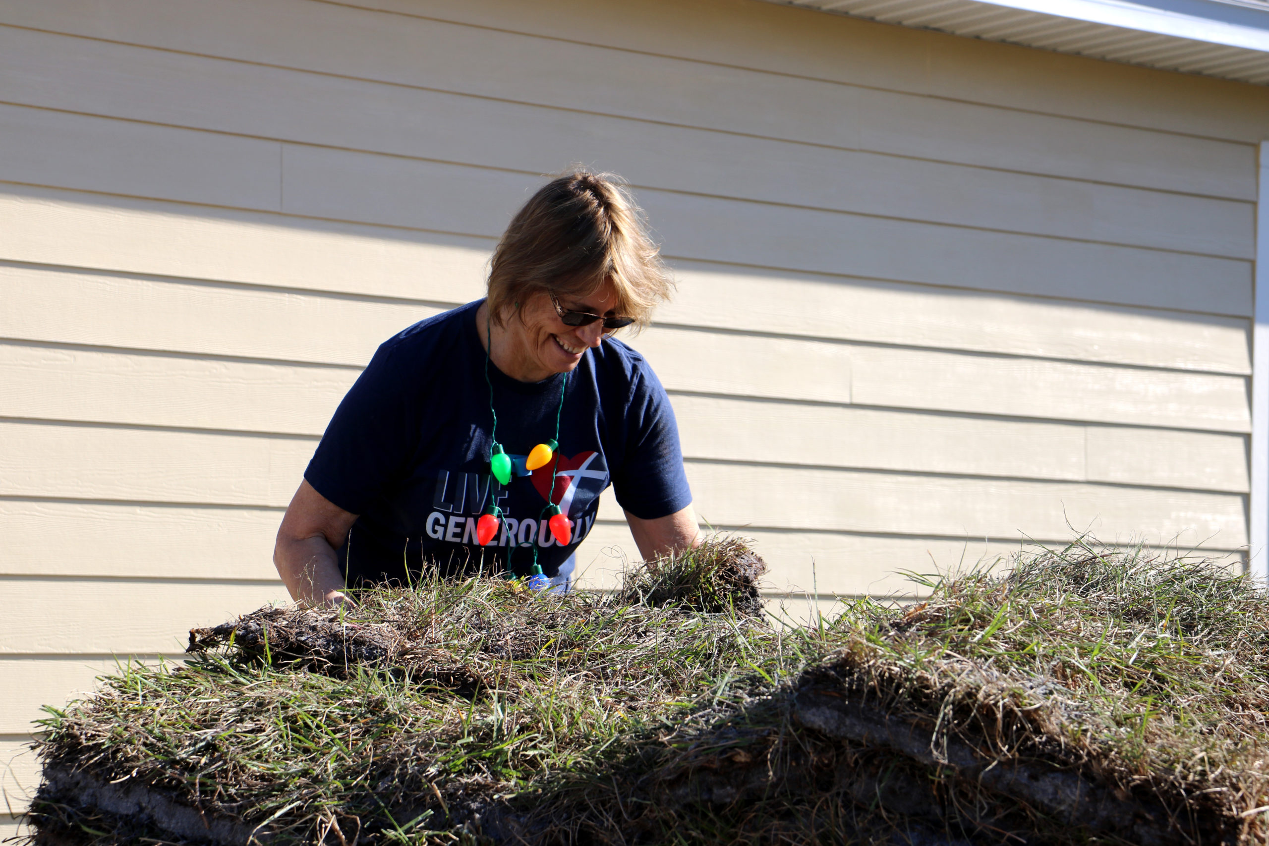 Volunteer smiling and reaching down to lift sod from pile