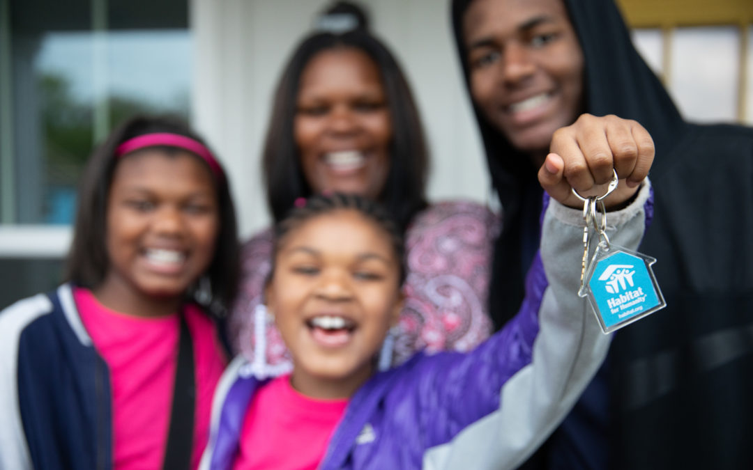 A child holds up a set of keys while another child, a woman and a teen smile behind her.