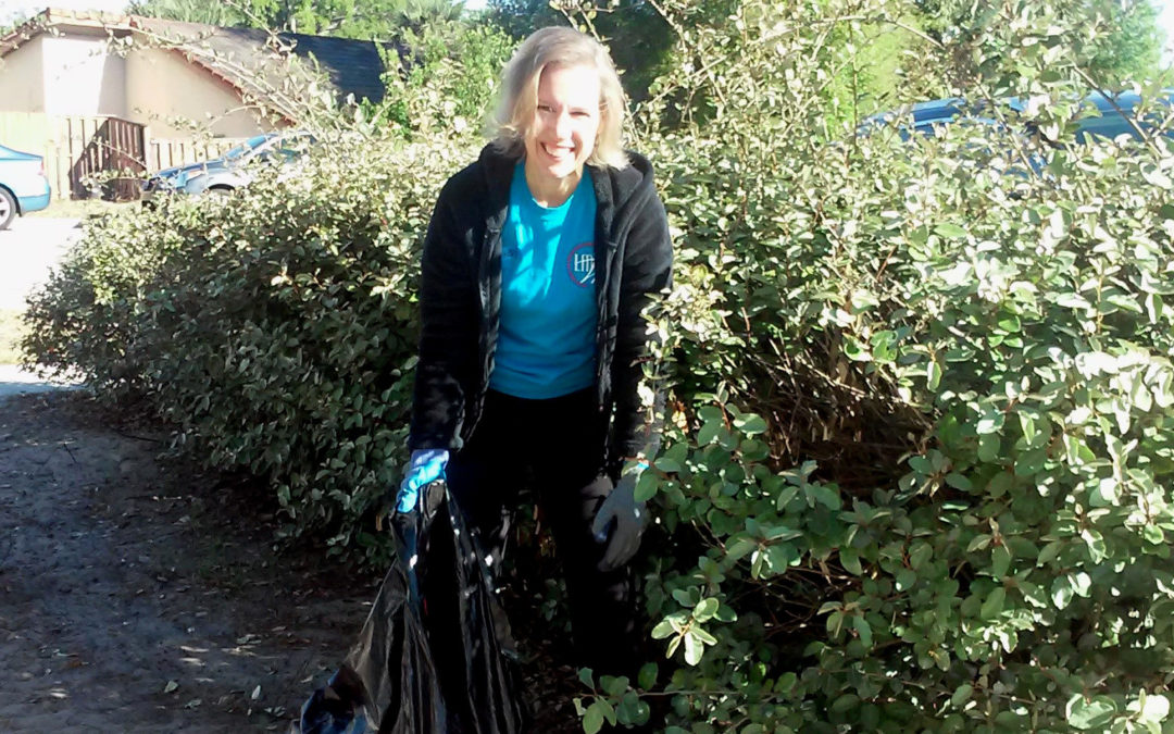 A woman smiles at the camera while holding a trash bag.