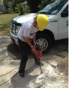 A woman uses a jack hammer on a sidewalk.