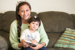 Uma mãe e seu filho sorriem para a câmera de seu sofá