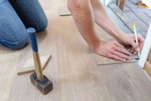 A person takes measurements as he or she lays flooring. 