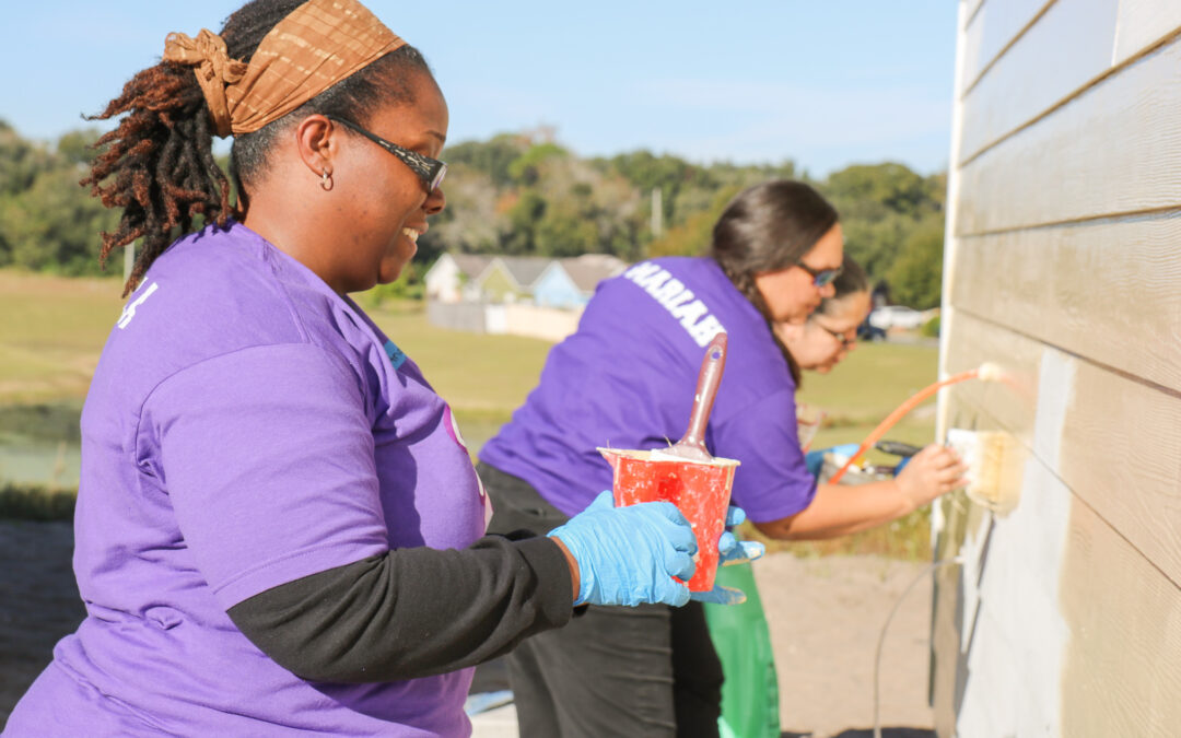 Three volunteers wearing Universal Orlando T-shirts paint a home.